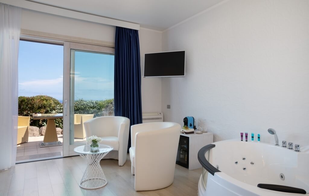 Modernes, minimalistisches Badezimmer mit Badewanne, Glas-Schiebetüren und Blick auf eine grüne Terrasse unter blauem Himmel.