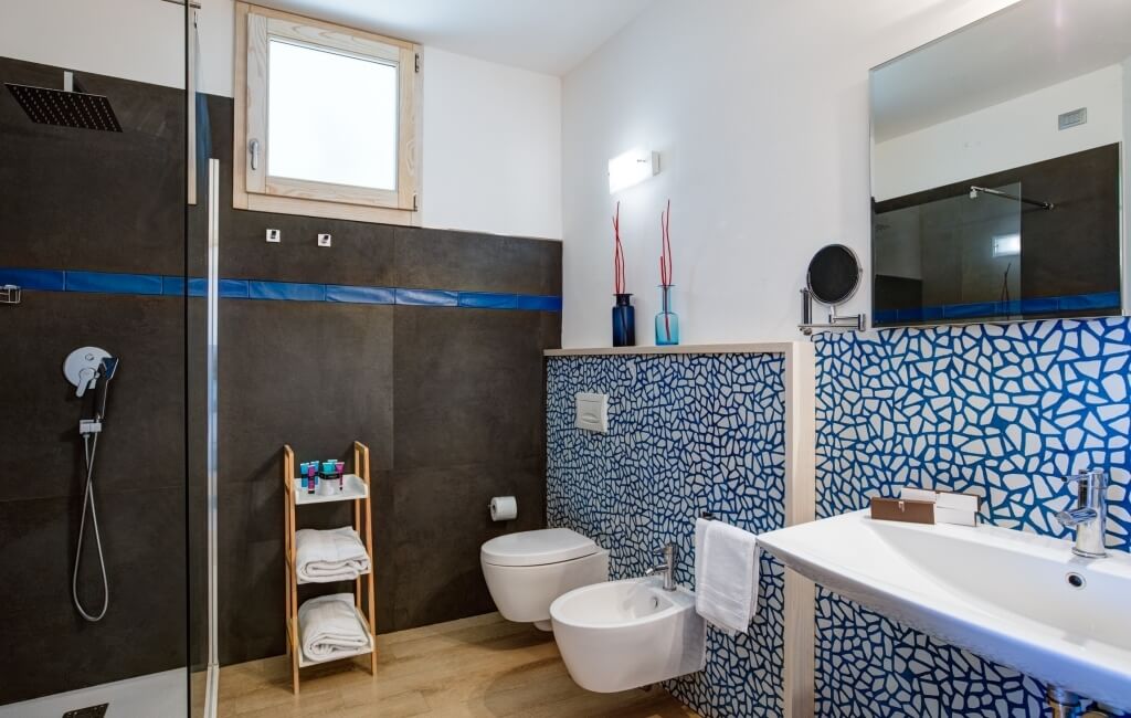 Modernes Badezimmer mit Dusche, Toilette, Waschbecken, Holzregal und mosaikverzierten Wänden. Helle, saubere Atmosphäre.