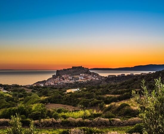 Serene coastal sunset over a small town on a hill, with lush greenery and a peaceful atmosphere.