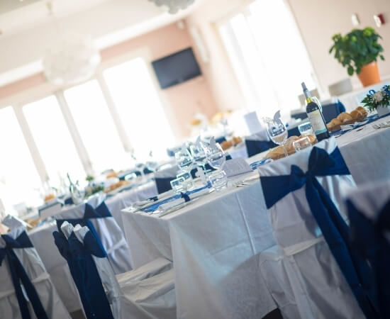 Impostazione formale per una cena con tavoli bianchi, tovaglie, bicchieri, piante e un'atmosfera elegante.