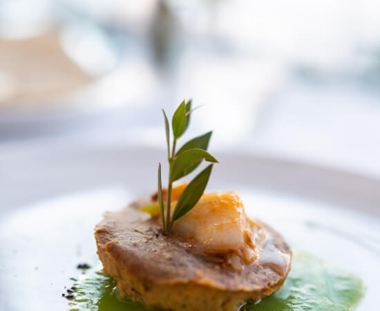 Scampo o capesante su una fetta di pane, guarnito con una piccola foglia verde, in un ambiente elegante e sfocato.