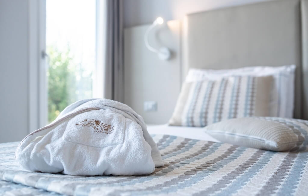 Ein einladendes Schlafzimmer mit einem Bett, einem gefalteten weißen Bademantel und einem Fenster, das natürliches Licht hereinlässt.