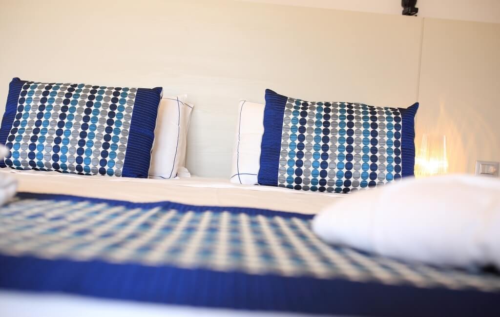 Bett mit blau-weißem gemustertem Bettbezug, passenden Kissen und zusätzlichen weißen Kissen vor einer cremefarbenen Wand.