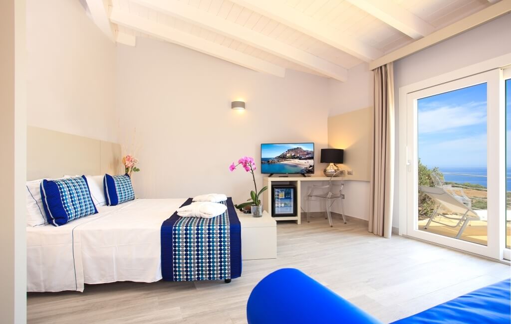 Ein modernes Hotelzimmer mit Doppelbett, TV, Schreibtisch und Balkon mit Meerblick, in ruhigen Farben und sauberem Design.