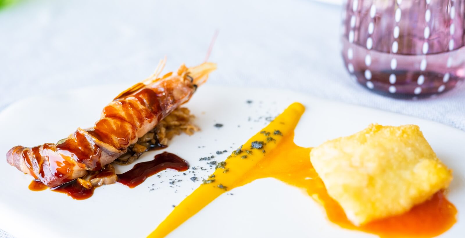 Gros plan sur une brochette de crevettes enroulée de bacon, accompagnée de sauces jaune et marron, sur un lit de chou.