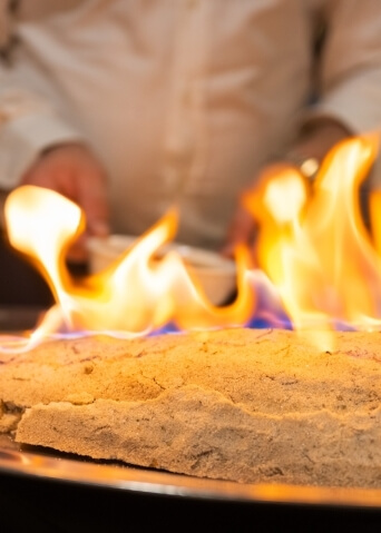 Superficie rotonda con fiamme giallo-arancio e blu, mentre una persona in camicia bianca tiene una ciotola.