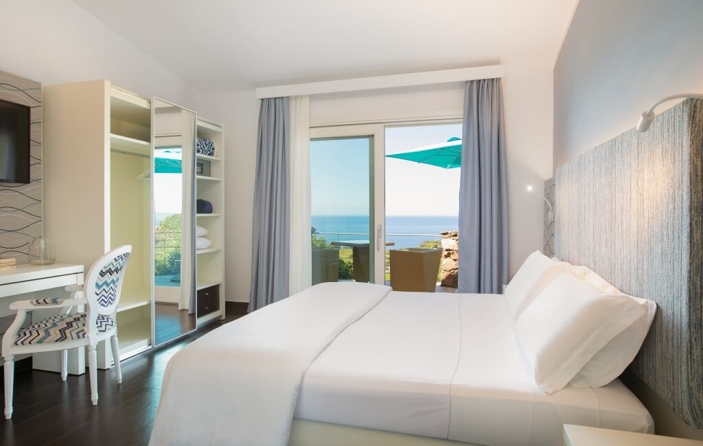 Ein stilvolles Schlafzimmer mit Meerblick, einem gemütlichen Bett, Leseecke und Arbeitsplatz, strahlt Ruhe und Eleganz aus.