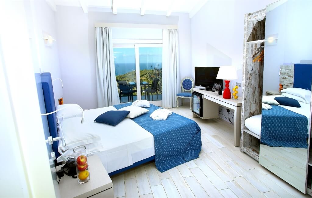Ein modernes Hotelzimmer mit einem Bett, Schreibtisch, Fernseher und einer Schiebetür zum Balkon, in minimalistischer Dekoration.