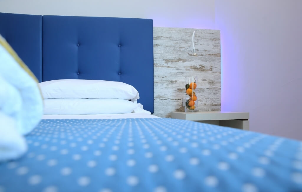 Ein einladendes Schlafzimmer mit einem blauen Bett, weißen Bettwäsche, einem Nachttisch mit Orangen und sanfter Beleuchtung.