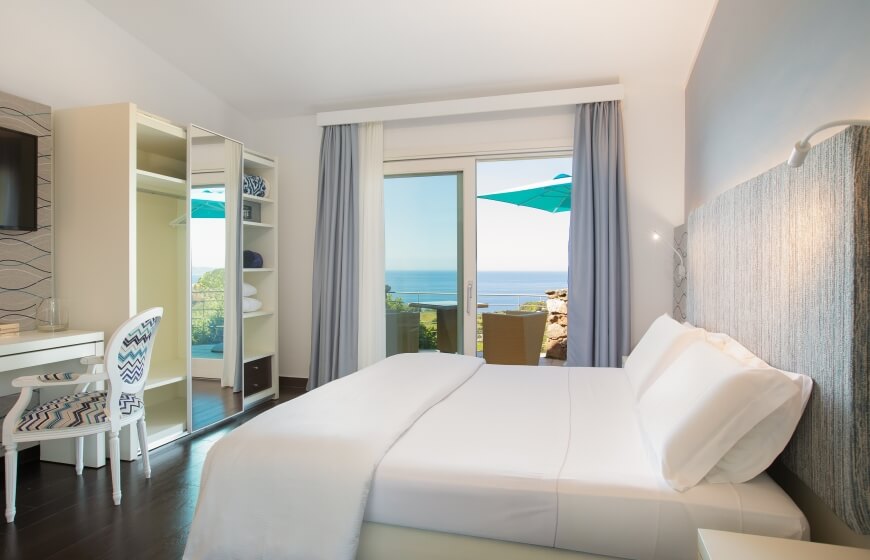 Chambre sereine avec vue sur l'océan, lit blanc, décor apaisant et lumière naturelle, créant une ambiance relaxante.