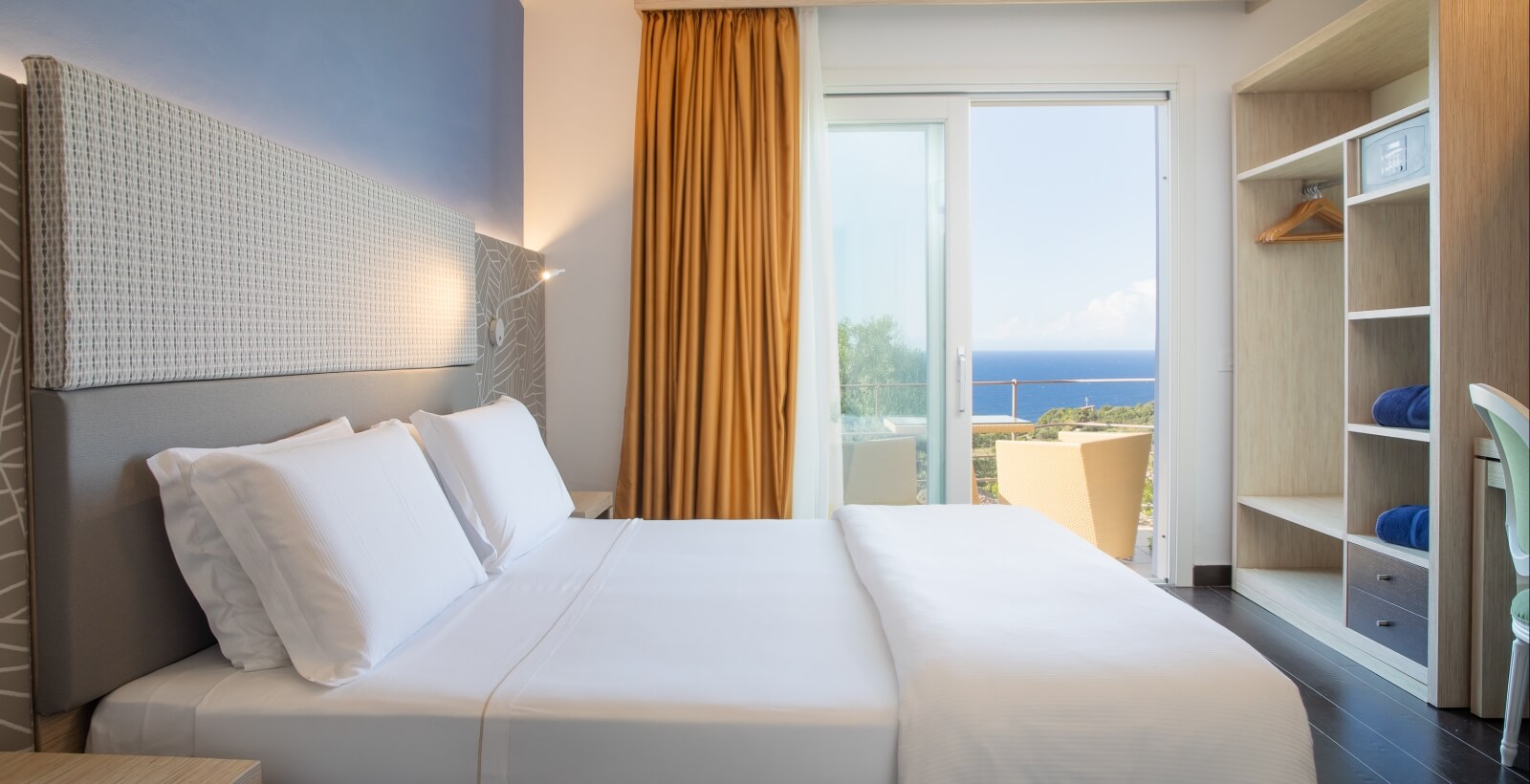 Camera d'hotel accogliente con letto, comodino, armadio e vista sull'oceano da una porta scorrevole aperta.