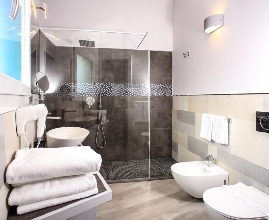 Modern bathroom with shower, toilet, sink, gray-brown floors, and white walls; towels and mirror included.