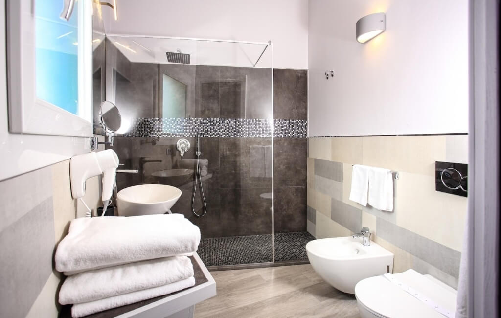 Modern bathroom featuring a glass shower, white sink and toilet, stacked towels, and stylish lighting.