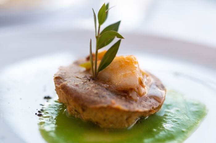 Un souffle su una salsa verde, guarnito, su un piatto bianco in un ambiente sfocato.