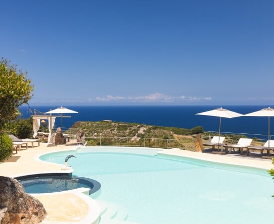 Luxuriöser Außenpool mit Hot Tub, Liegen und Pavillon auf einer Klippe mit Blick auf den Ozean unter klarem Himmel.