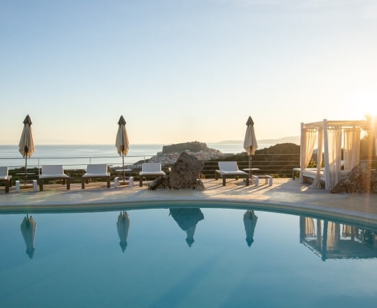 Ein einladender Pool mit Blick auf den Ozean, umgeben von Liegen, Sonnenschirmen und einer Pergola, strahlt Ruhe aus.