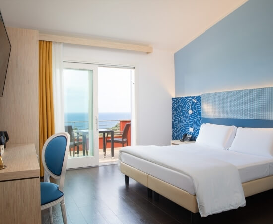 Moderne Hotelzimmer mit Meerblick, Balkon, Queen-Size-Bett, eleganten Möbeln und blauen Wänden.
