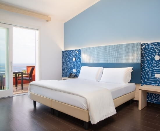 Modernes Schlafzimmer mit Bett, Nachttisch, und Schiebetüren zur Terrasse; beruhigende blaue und weiße Farbgestaltung.