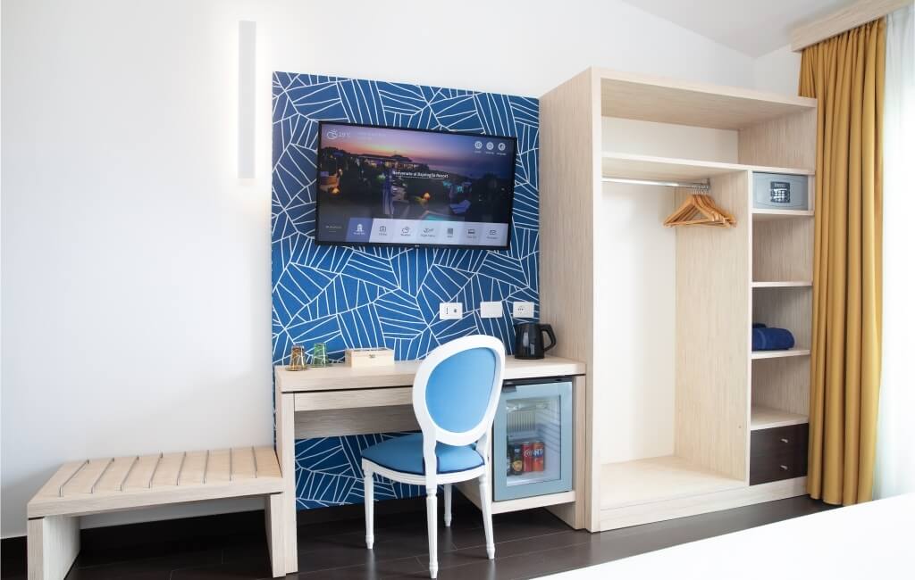 Modernes Hotelzimmer mit Schreibtisch, Fernseher, geometrischer Akzentwand in Blau und Weiß, und weiteren Annehmlichkeiten.