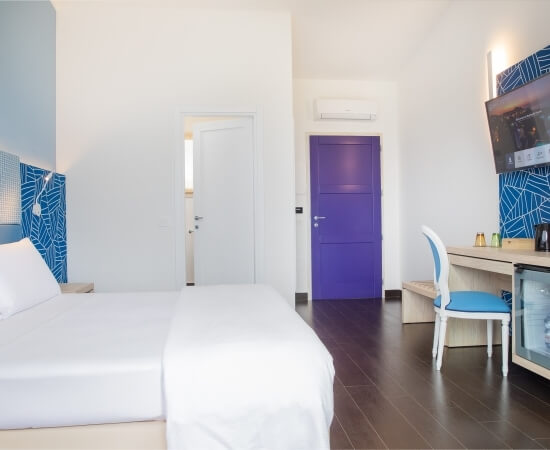 Modernes Hotelzimmer mit minimalistischer Ästhetik, weißer Wand, dunklem Holzboden, blauer Akzentwand und lila Tür.