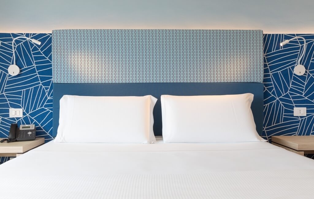 Hotelzimmer mit einem gemachten Bett, Nachttischen, blauen Wänden und geometrischen Mustern, einladend und sauber.