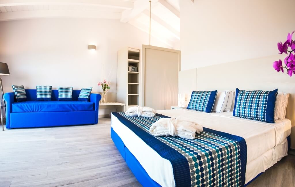 Ein gut gestaltetes Hotelzimmer mit einem Bett, einer Couch, Blumen und eleganten Dekorationen in hellen Farben.