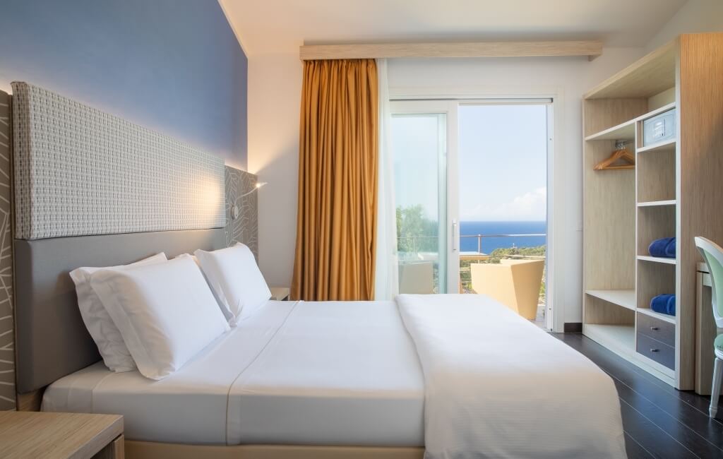 Ein ruhiges Hotelzimmer mit Doppelbett, Balkonblick auf das Meer und stilvollem Interieur in sanften Grautönen.