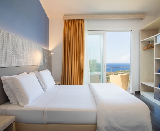 Camera d'hotel moderna con vista serena sul mare, letto matrimoniale, pareti bianche e accento blu, atmosfera rilassante.