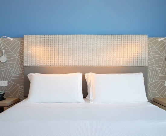 Camera da letto moderna con letto centrale, comodini, lampade e parete blu con motivo geometrico marrone e beige.