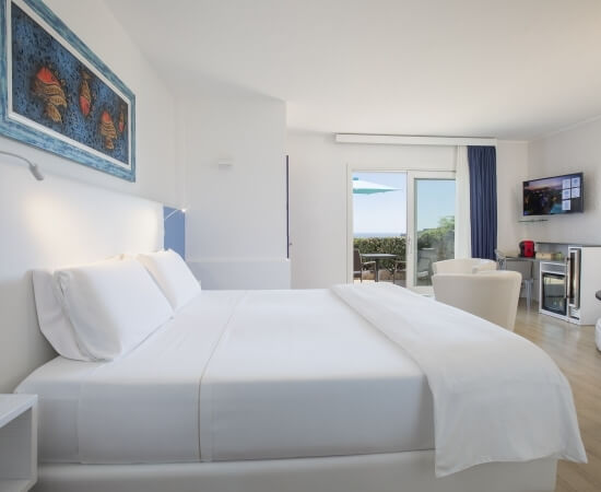 Modernes, minimalistisches Hotelzimmer mit großem Bett, blauen Wänden, Kunstwerk, und Zugang zu einer Terrasse.