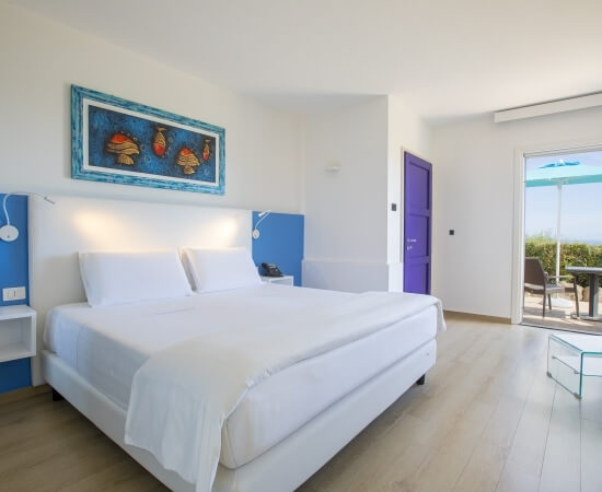 Ein einladendes Schlafzimmer in Weiß mit blauen und lila Akzenten, Glasdoor zur Terrasse und einem bunten Schmetterlingsgemälde.