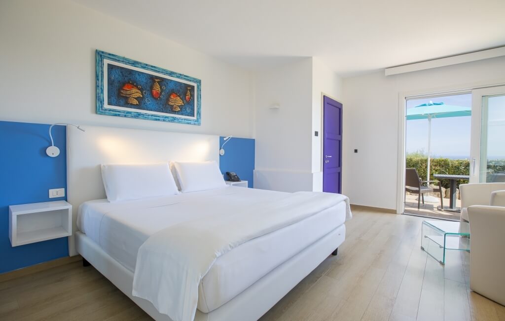 Modernes Schlafzimmer mit Balkon, großer Bett, Tisch und Stuhl, Glas-Couchtisch und blauer Blumenmalerei an der Wand.