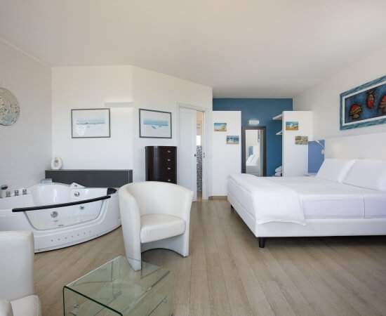 Modernes, minimalistisches Hotelzimmer in Weiß und Blau mit einem großen Bett, Badezimmer und eleganter Glas-Tisch.