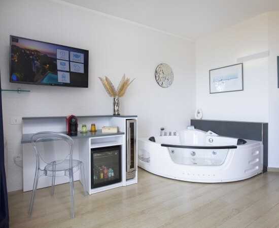 Innenansicht eines Hotelzimmers mit TV, Kücheninsel, Jacuzzi und Wandgemälde.