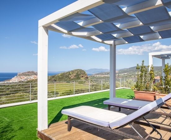 Zwei weiße Liegestühle unter einer Pergola mit Blick auf eine malerische Landschaft mit Hügeln und Wasser.
