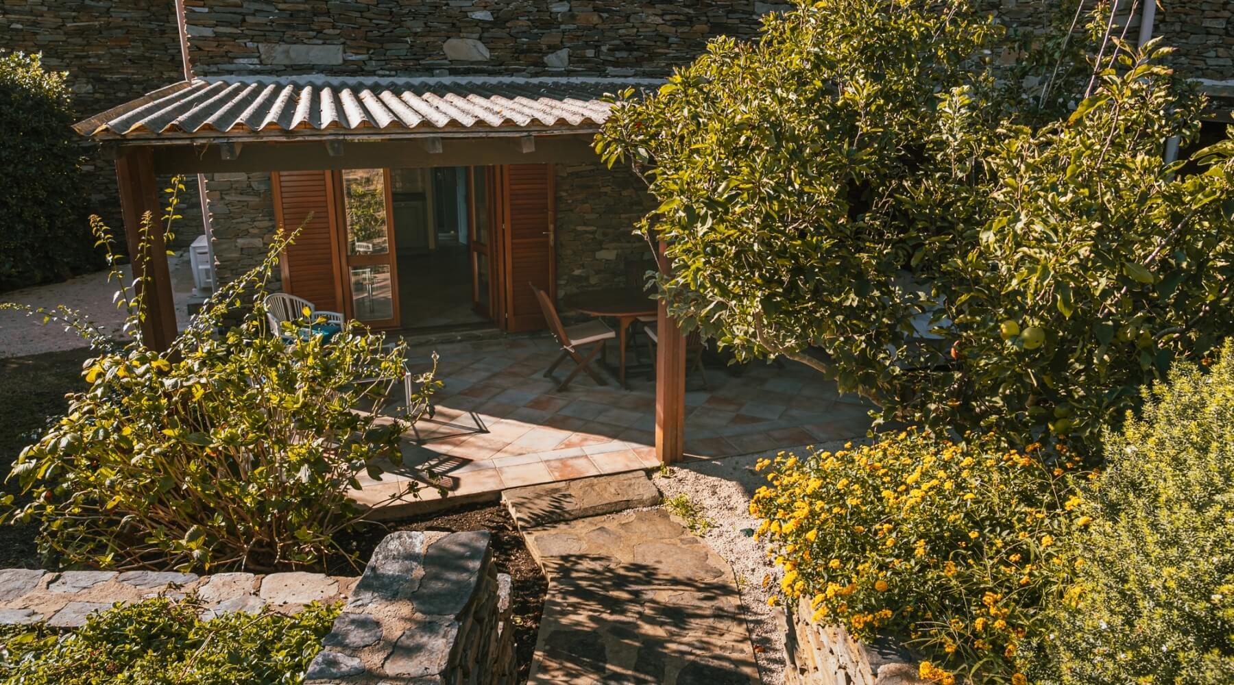 Patio con tavoli, piante, muro di pietra e sentiero.