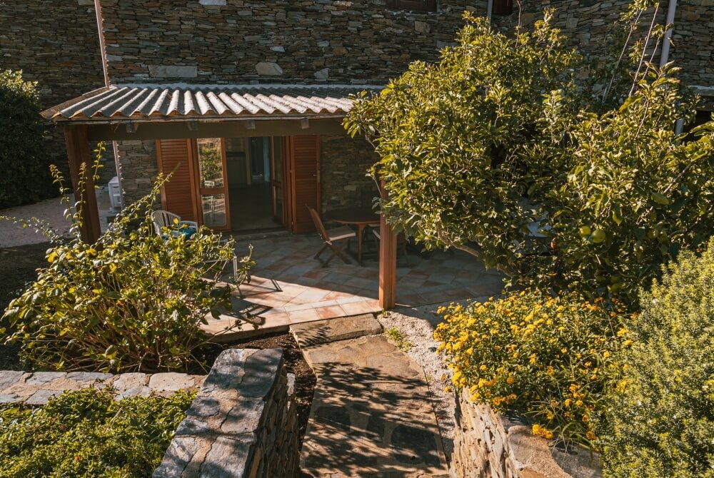 Edificio in pietra con patio coperto e giardino fiorito.