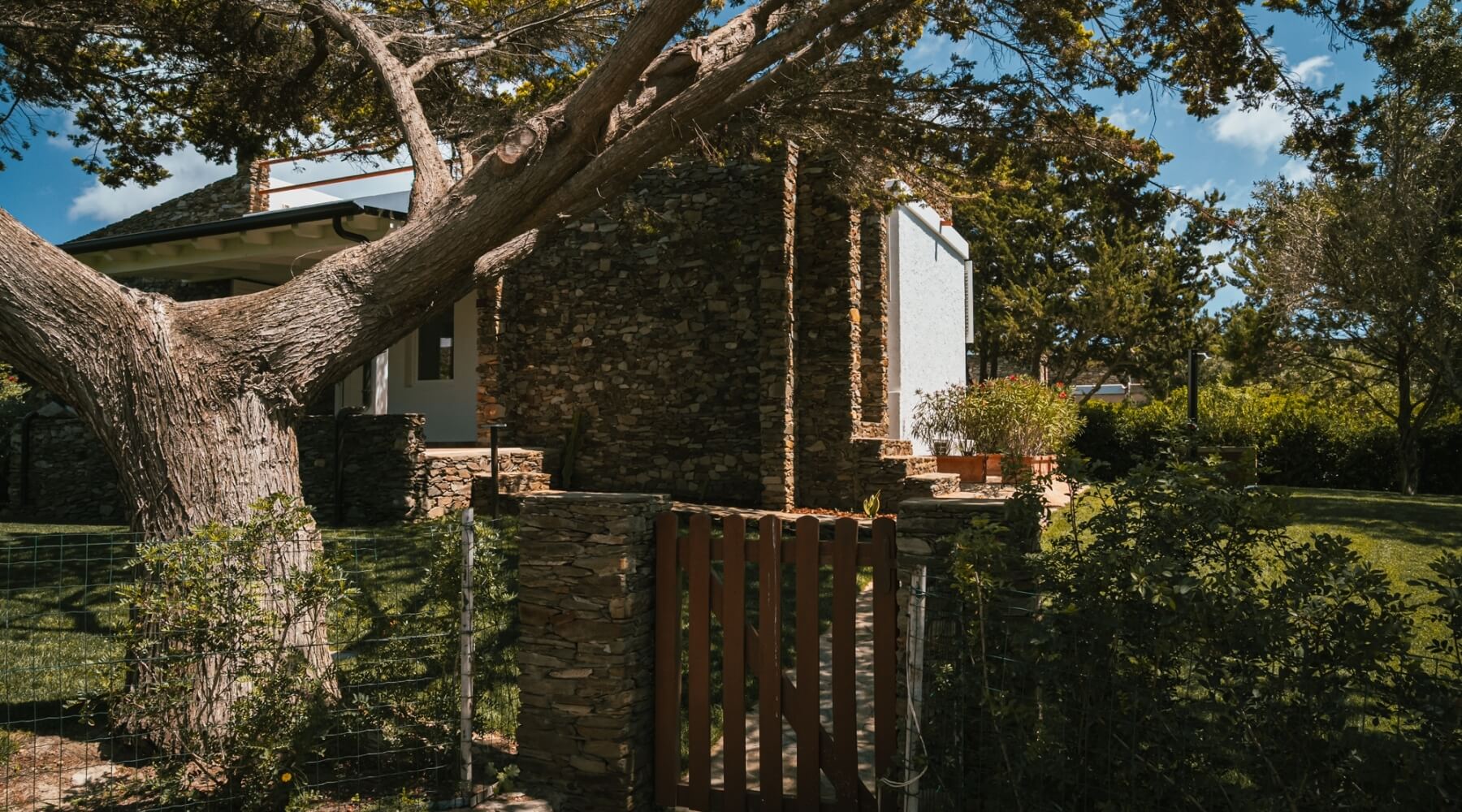 Edificio in pietra con alberi, cancello di legno e cielo blu.