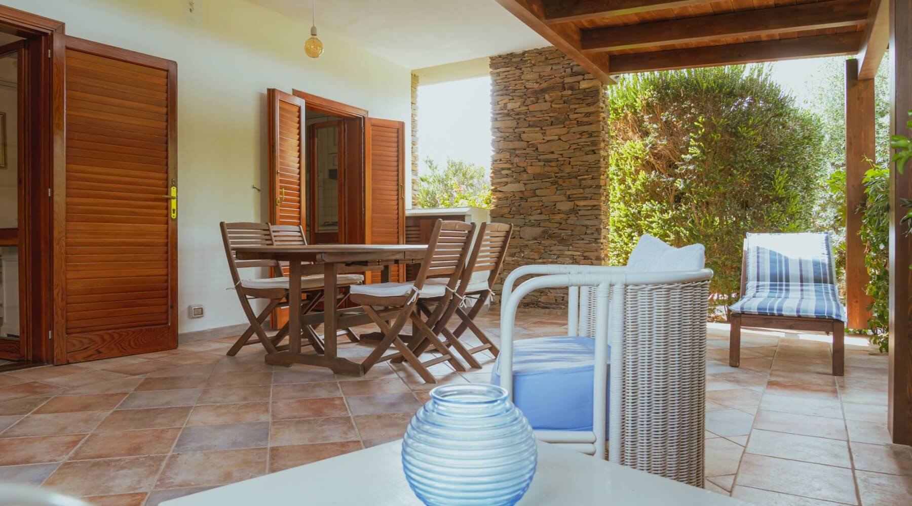 Patio con tavolo in legno, sedie e piante verdi.