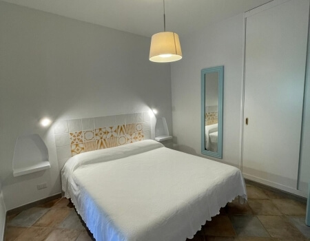 Camera d'hotel con letto bianco, specchio e armadio bianco.