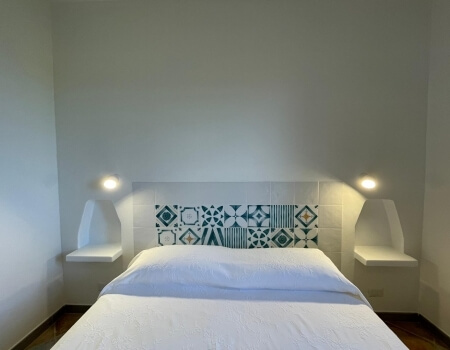 Camera d'hotel con letto, testata decorata e mensole illuminate.