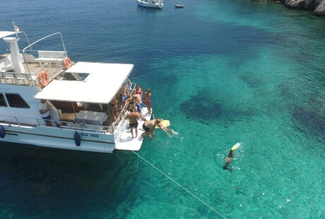 Una barca bianca su acqua turchese con persone che nuotano.