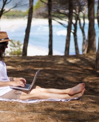 Persona seduta all'aperto, usando un laptop con alberi e acqua sullo sfondo.