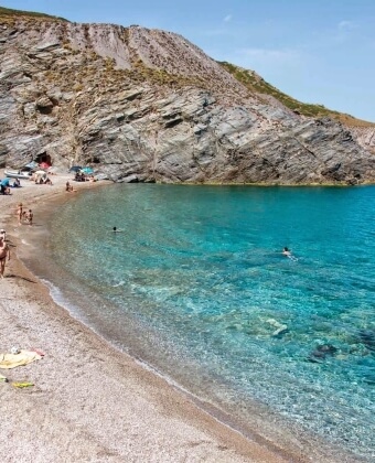 Cala rocciosa con acqua blu, persone che nuotano e prendono il sole.