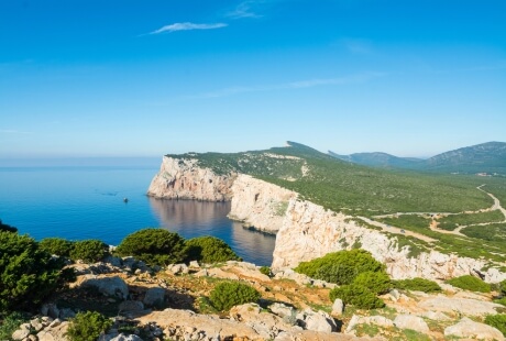 Cliffs and green vegetation under a bright blue sky.   **Italian:** Scogliere e vegetazione verde sotto un cielo blu brillante.
