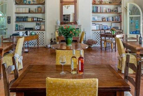 Area pranzo con tavoli in legno, bottiglie di vino e piante.