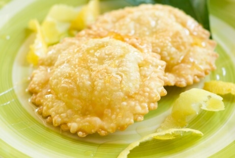 Due dolci fritti dorati con sciroppo, limoni e scorza.