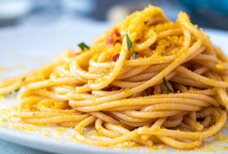 Piatto di spaghetti con crumble giallo e erbe verdi.