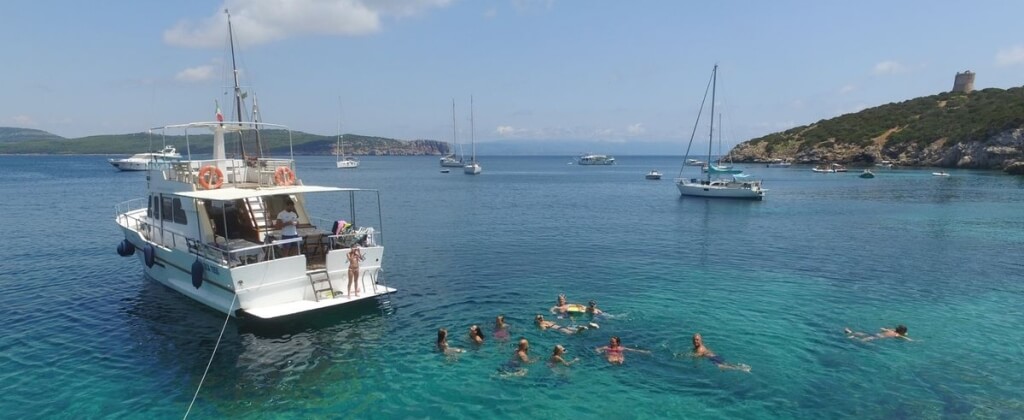 Barca bianca ancorata in acqua blu, persone nuotano intorno.