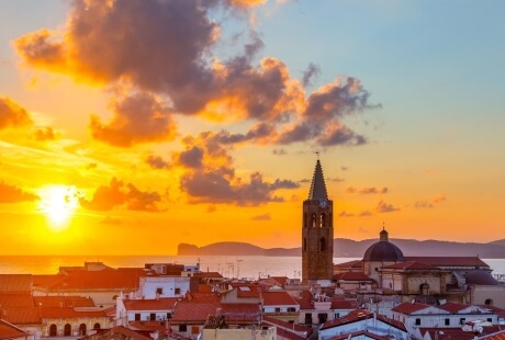 Vista aerea di un paese costiero al tramonto con un campanile.